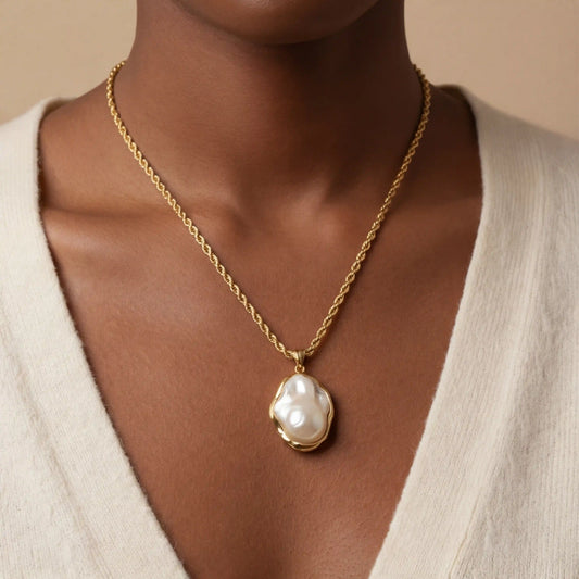 A stunning portrait of a model with a deeper skin tone wearing The Theia Necklace, showing the beautiful contrast of the white pearl and warm gold.