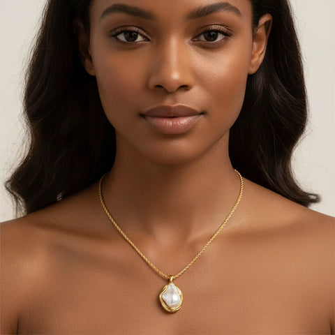 A stunning portrait of a model with a deeper skin tone wearing The Theia Necklace, showing the beautiful contrast of the white pearl and warm gold.