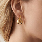 Close up of woman wearing chunky gold urban link earrings with square interlocking design.