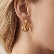 Close up of woman wearing chunky gold urban link earrings with square interlocking design.