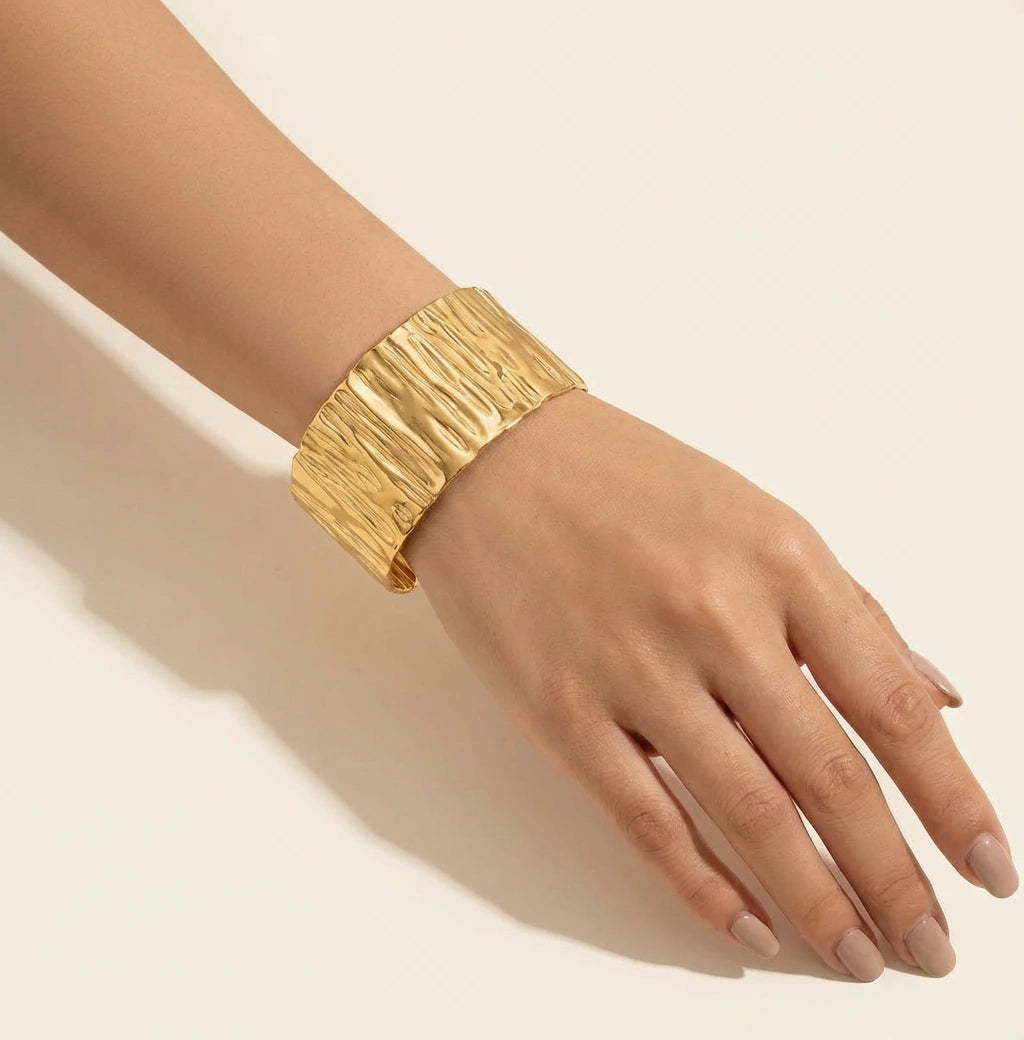 A woman wearing a wide gold textured bangle bracelet on wrist gives an elegant look.