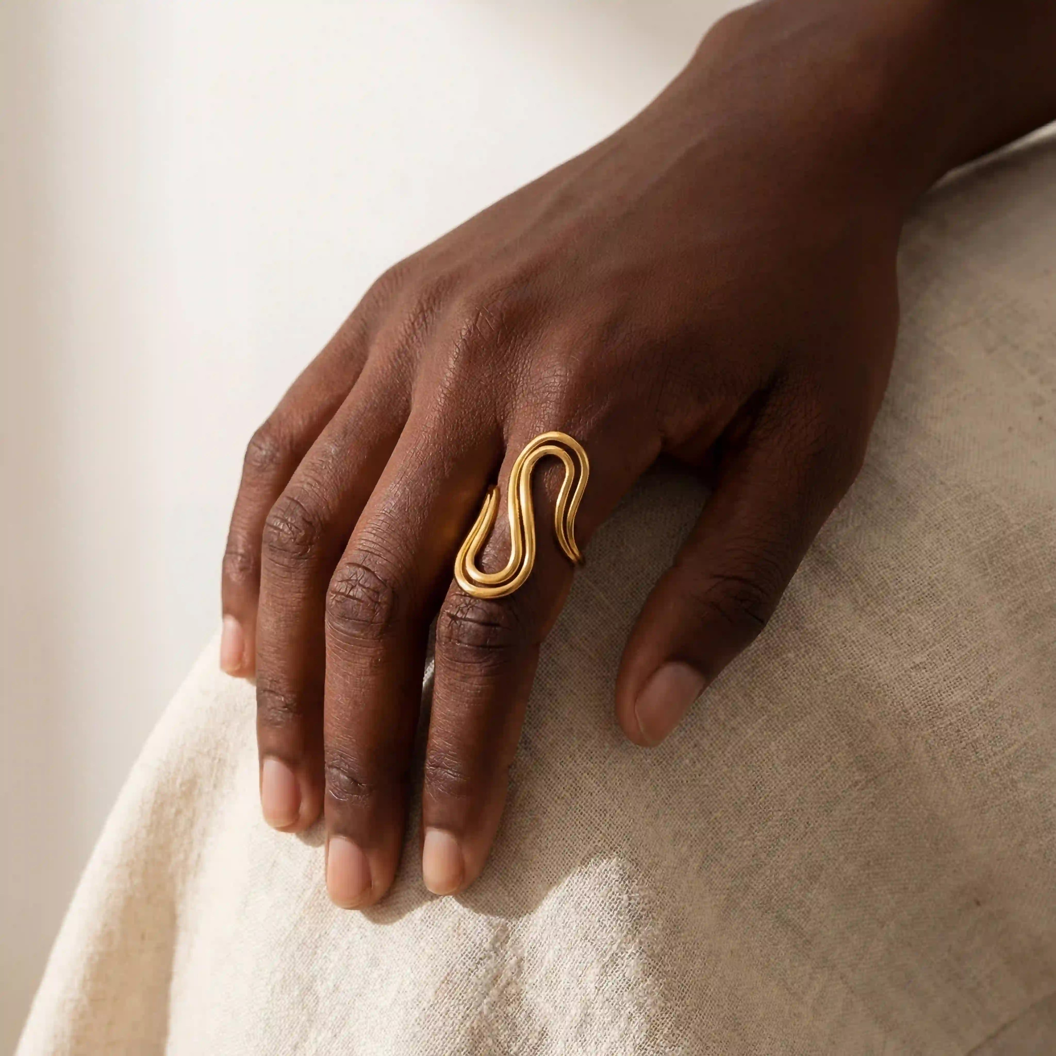 Dark skin model styling gold sculptural drift ring on index finger modern jewelry. Main image
