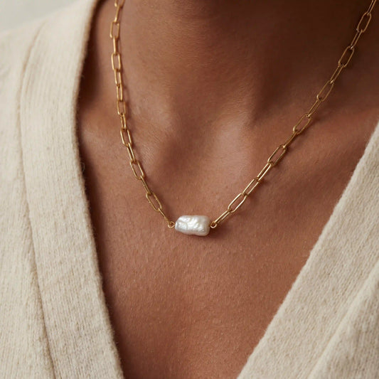 Close up of woman wearing gold paperclip chain necklace with organic baroque pearl pendant.