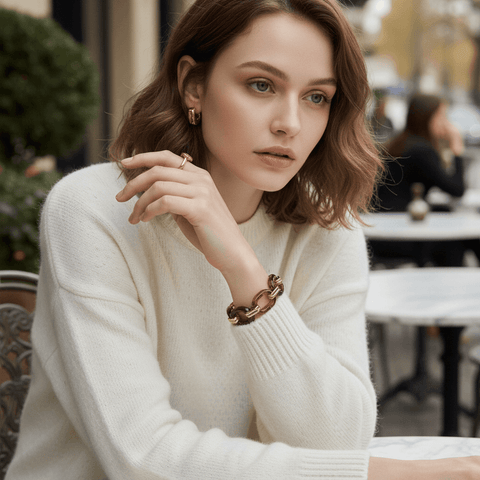 A chic model wearing the Florence tortoiseshell bracelet with a cozy white sweater, resting her chin on her hand while sitting at an outdoor European cafe.