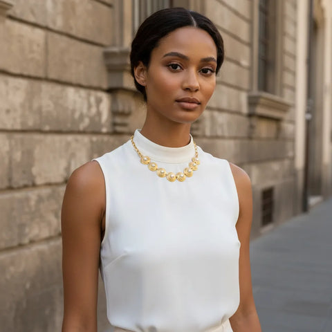 A chic model wearing The Hera Necklace with a modern, sleeveless white top, demonstrating its versatility as a powerful statement piece for a city look.