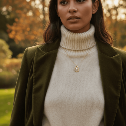 A detailed shot of a model's layered necklace stack, with The Luna Pearl necklace positioned as the shortest, most prominent piece. It acts as the classic, elegant anchor for other gold chains.